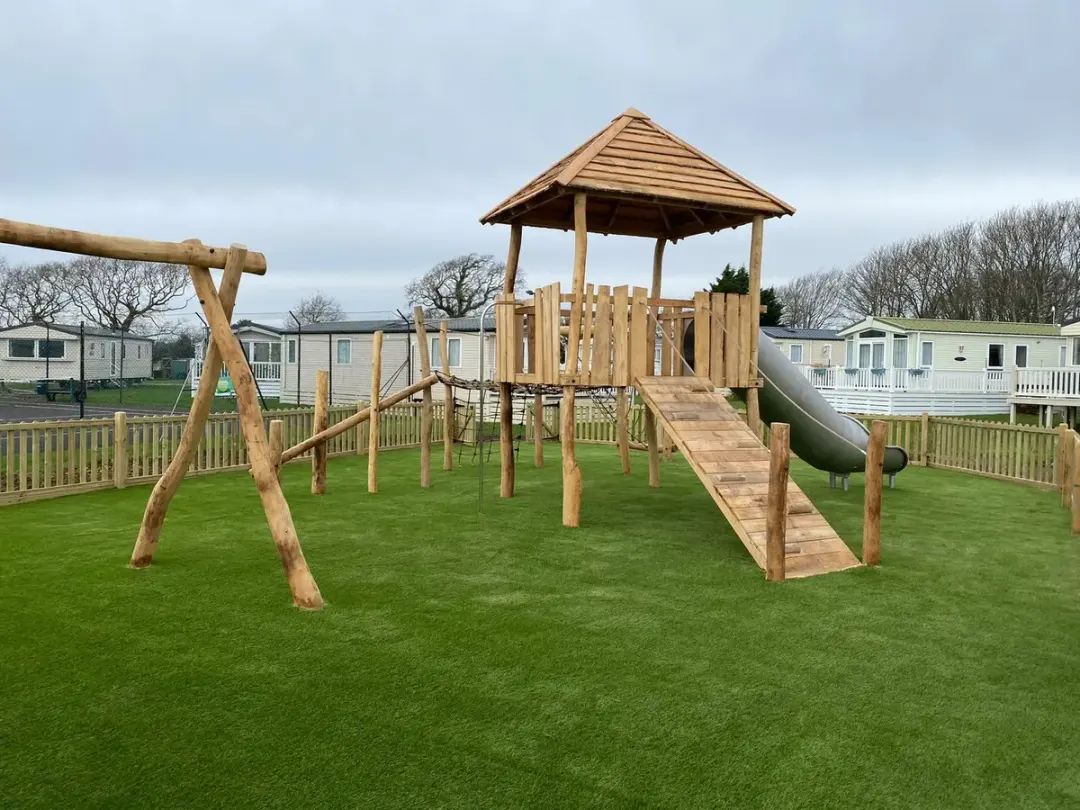 Natural timber play tower with slide, rope bridge and swings on artificial grass