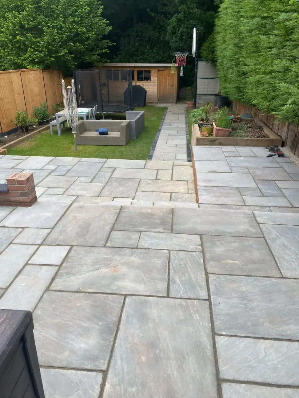 Grey natural sandstone patio with pathway, raised timber beds and lawn