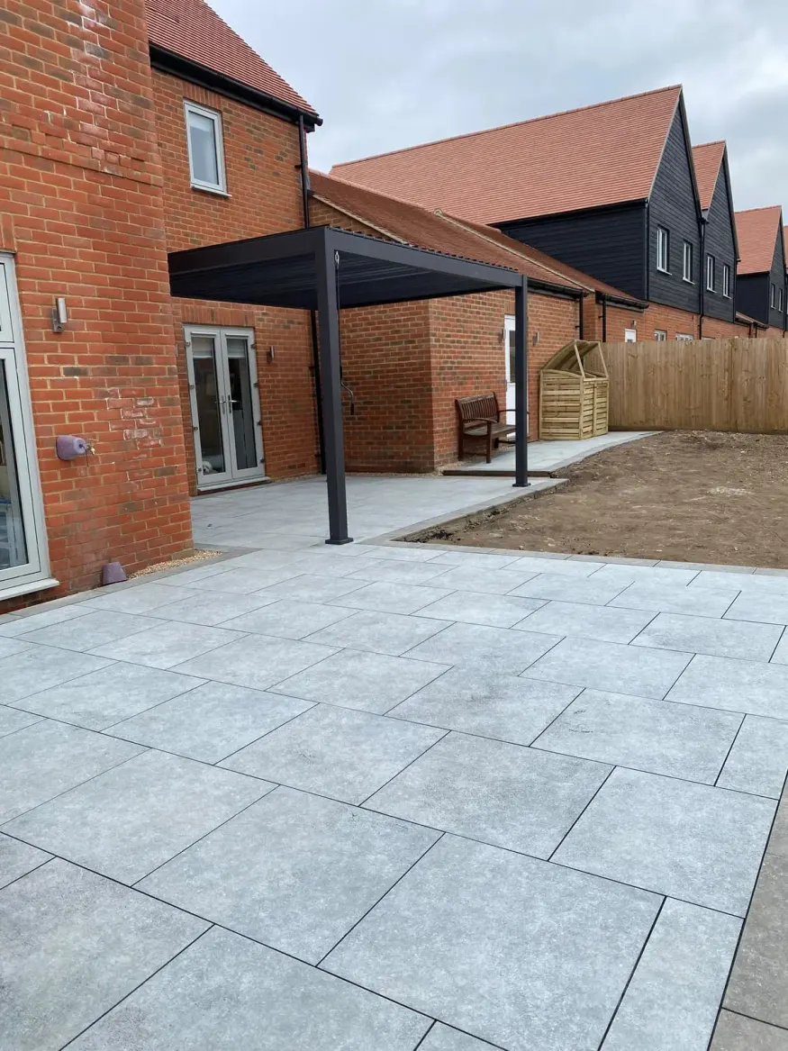 Grey porcelain patio under a modern aluminium canopy beside a brick house
