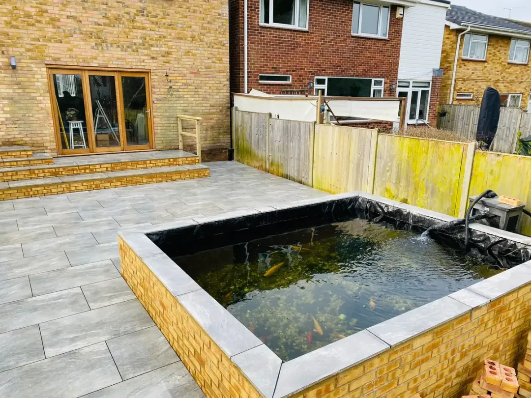 Brick raised fish pond with water feature set into a porcelain patio