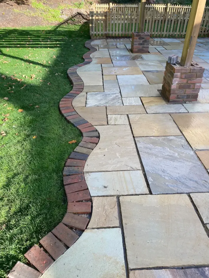 Sandstone patio with curved brick edging beside a lawn and pergola posts