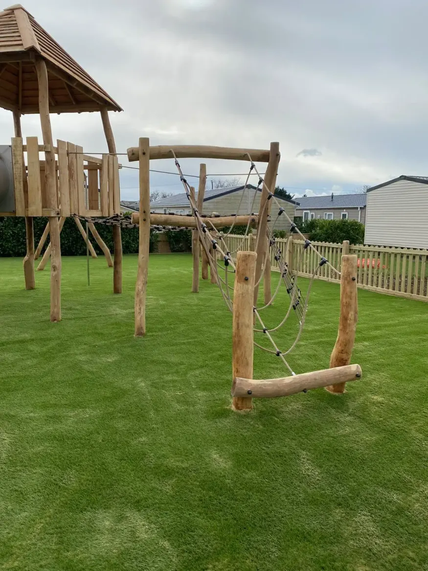 Timber play tower with rope climbing bridge and slide on artificial grass