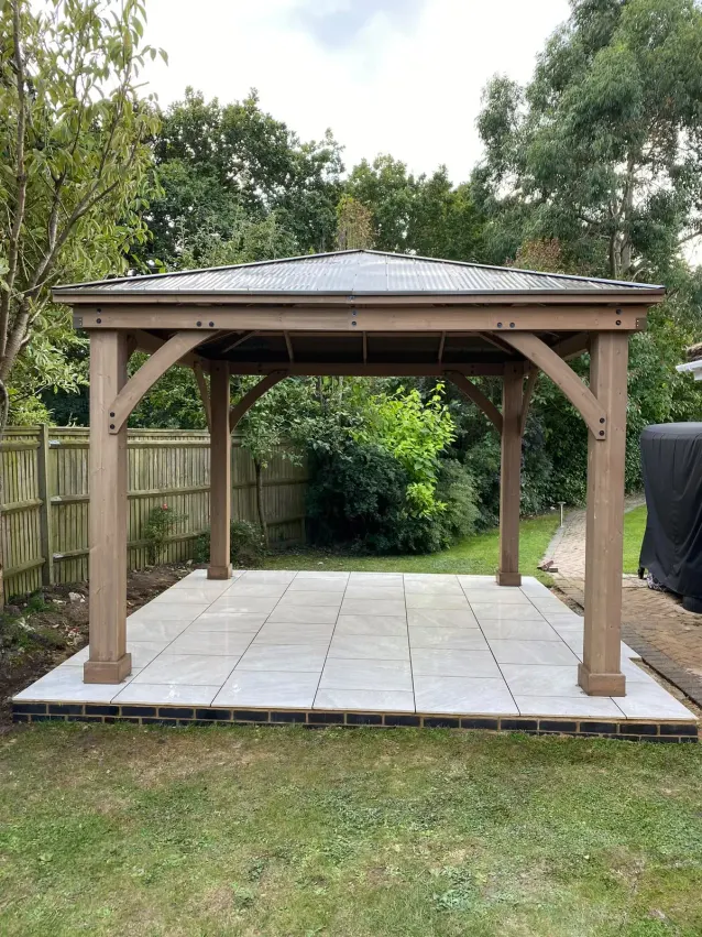 Timber gazebo standing on a new porcelain patio base in a lawned garden