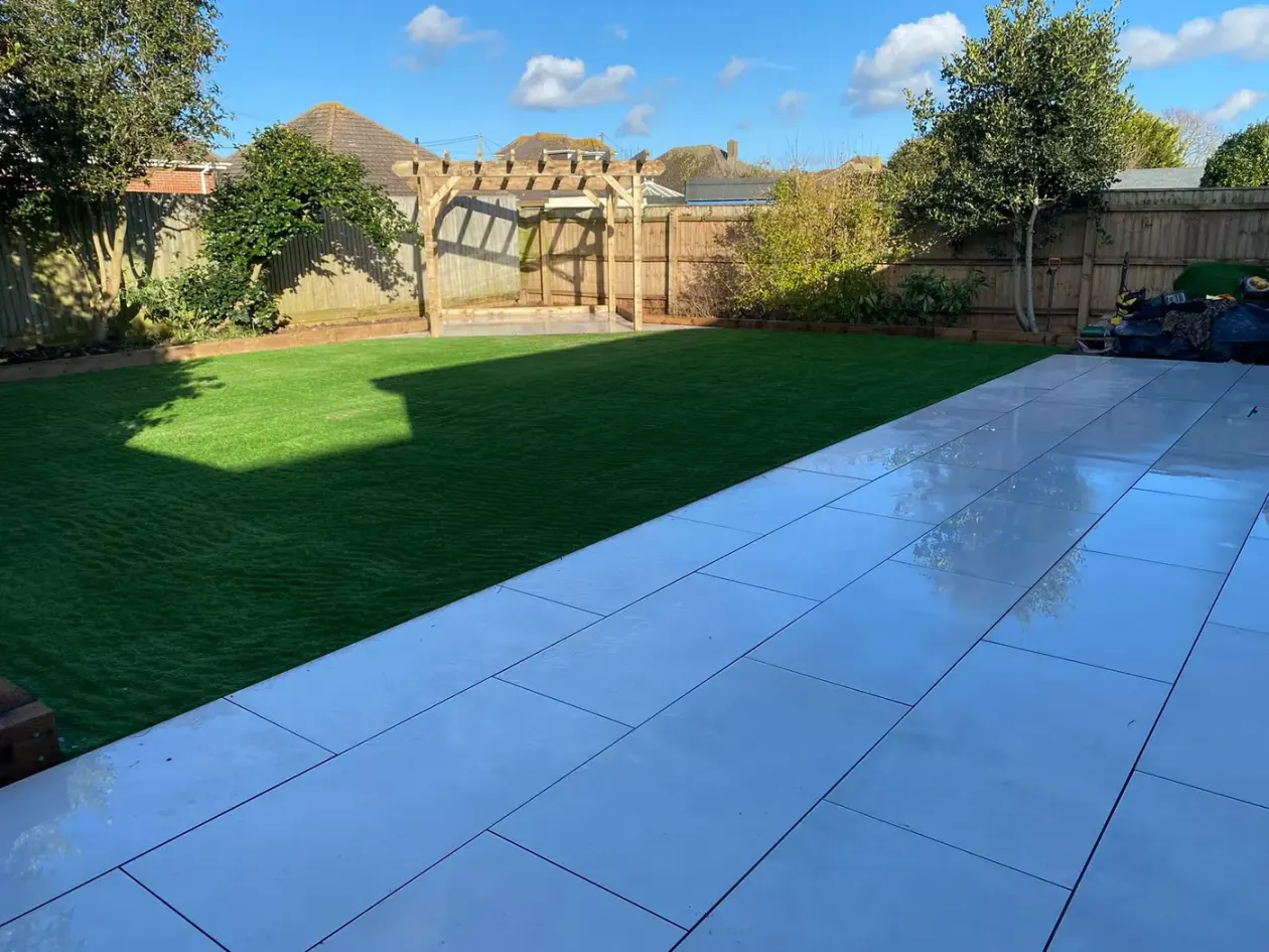 Long grey porcelain patio beside a fresh lawn with a pergola beyond