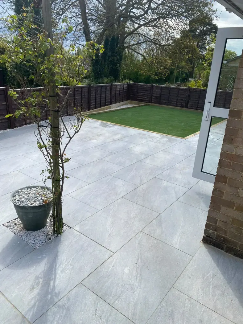 Light grey porcelain patio leading to an artificial lawn with a planted tree
