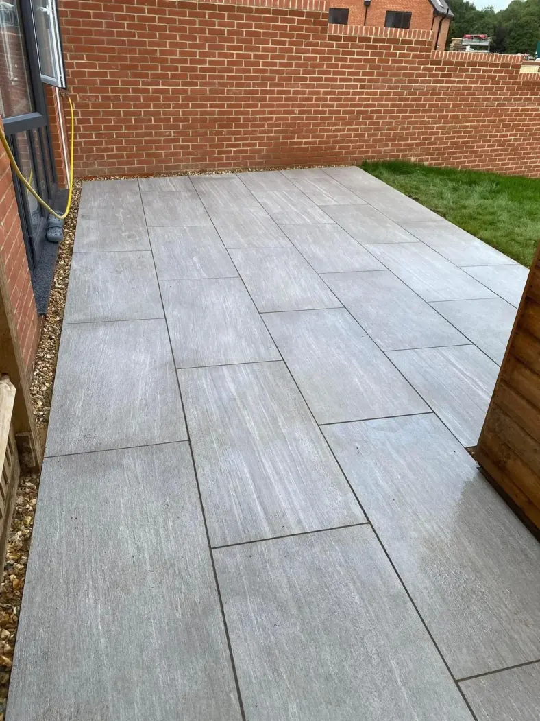 Wood-effect grey porcelain paving along the side of a brick house