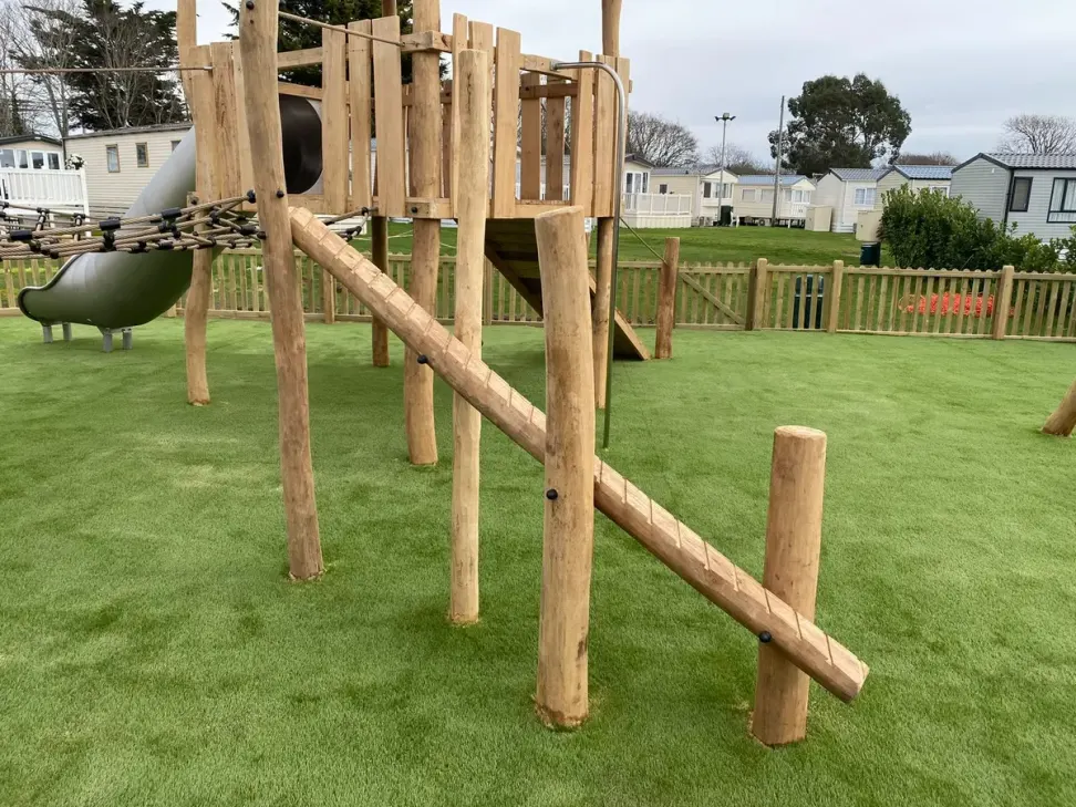 Timber play tower with tube slide and climb ramp on artificial grass